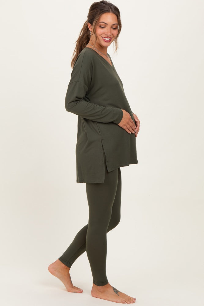 woman wearing a dark green maternity top and matching leggings, gently cradling her baby bump