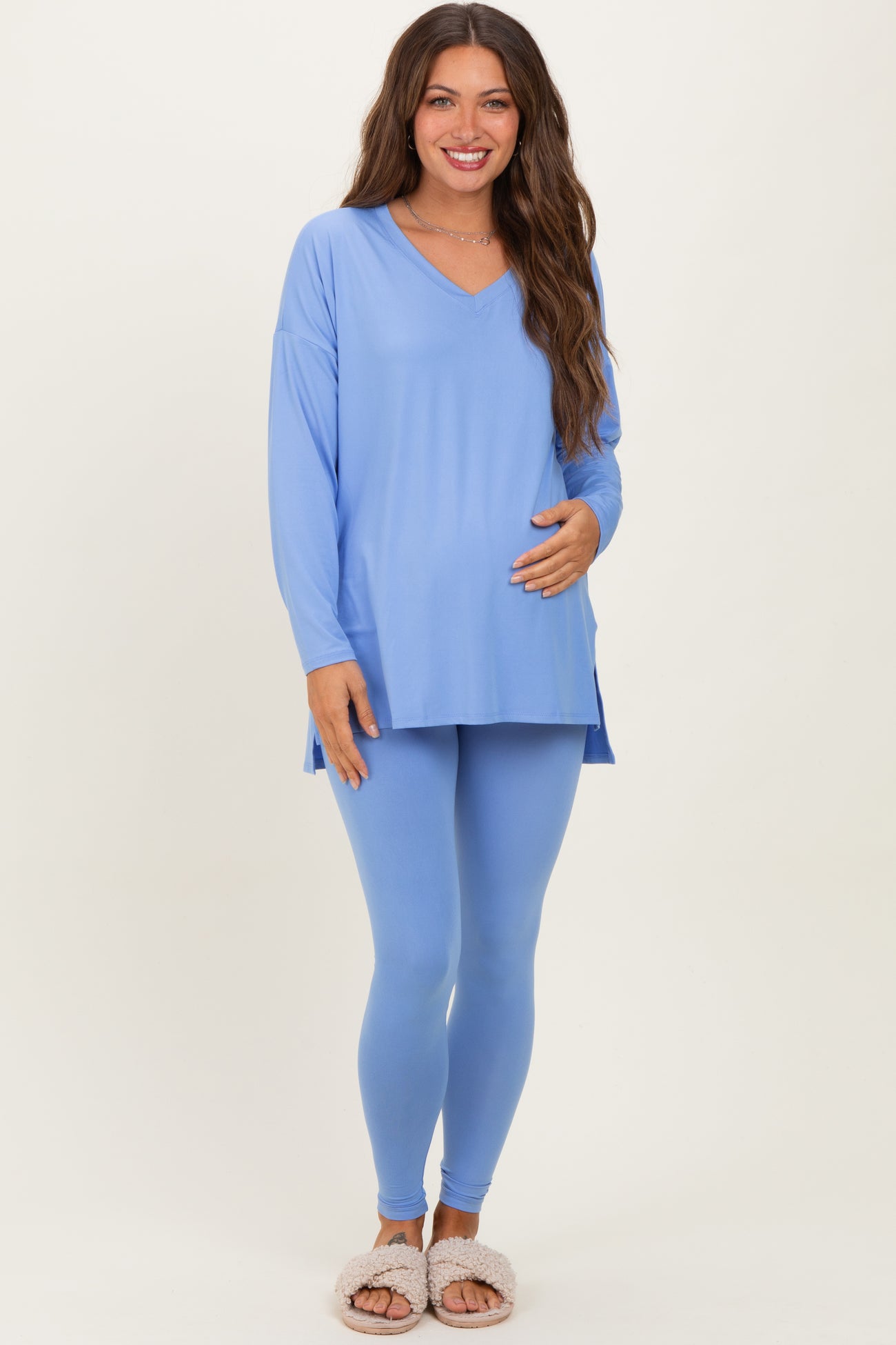 woman wearing a light blue long sleeve maternity top and matching leggings, holding her baby bump