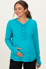 woman wearing a turquoise long sleeve maternity top with button details and holding her baby bump