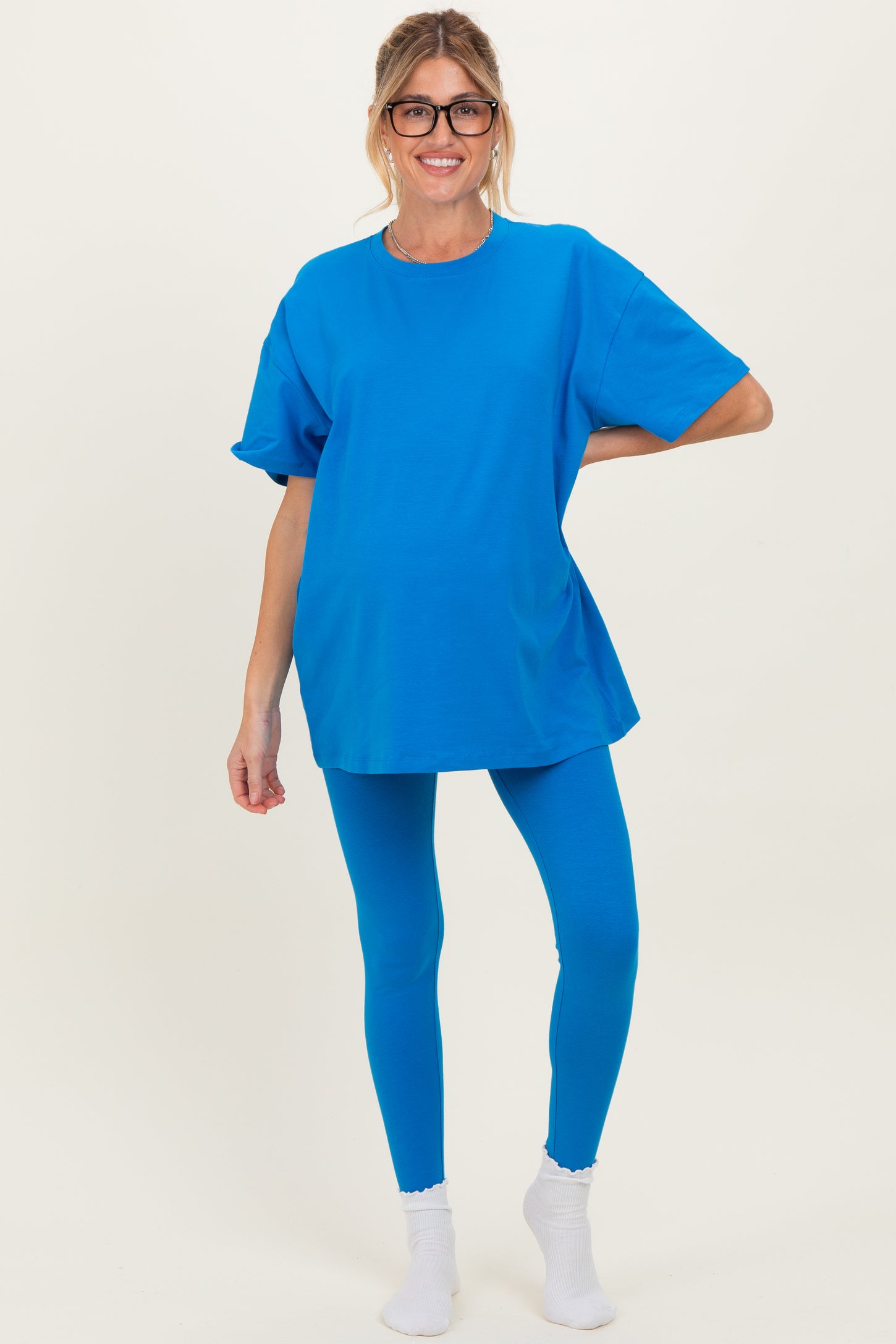 woman wearing a bright blue maternity t-shirt and matching leggings, posing with a baby bump visible