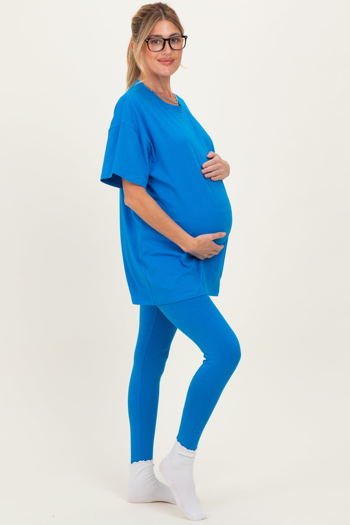 woman wearing a bright blue maternity t-shirt and matching leggings, holding her baby bump