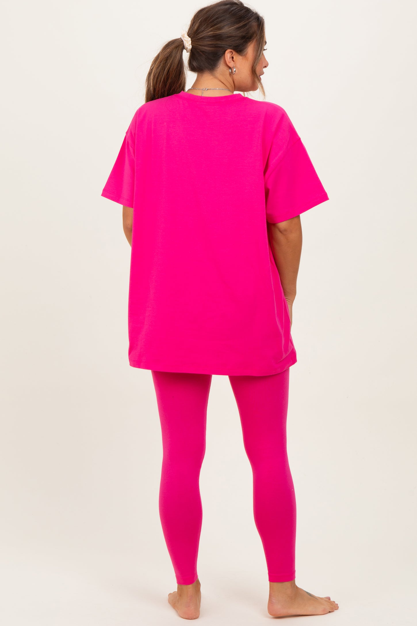 woman wearing a hot pink oversized t-shirt and matching leggings, showcasing a casual maternity outfit.