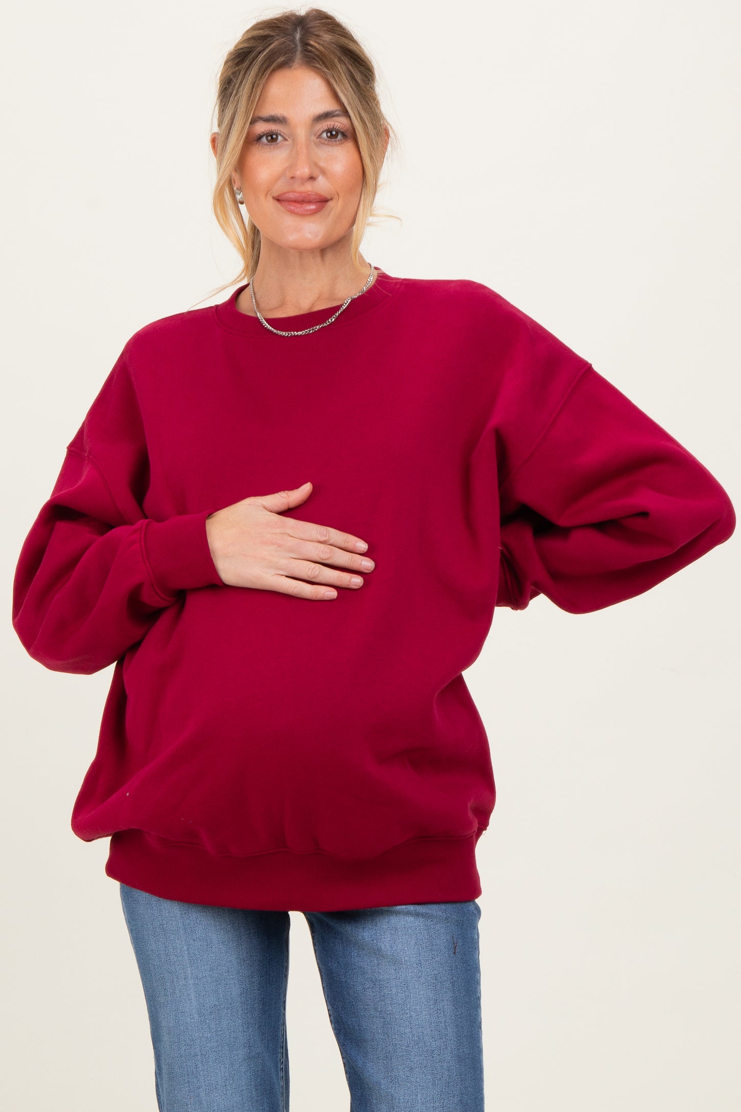 woman wearing a burgundy oversized maternity sweatshirt and holding her baby bump