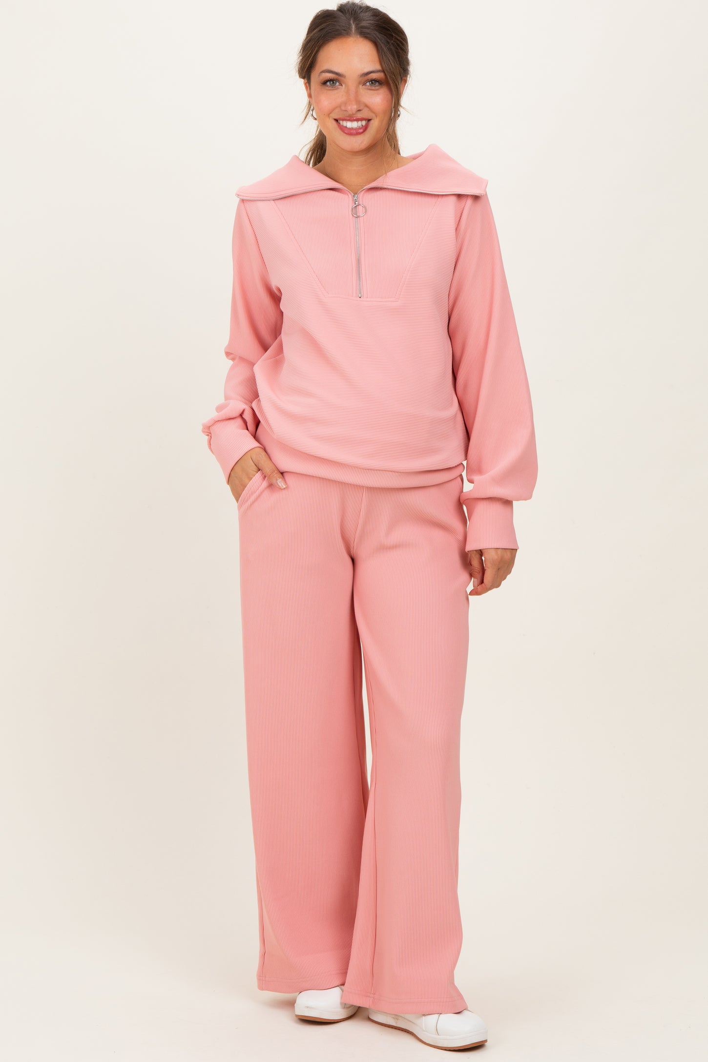 woman wearing a light pink ribbed maternity pullover with a collar and matching wide-leg pants, posing with hands in pockets