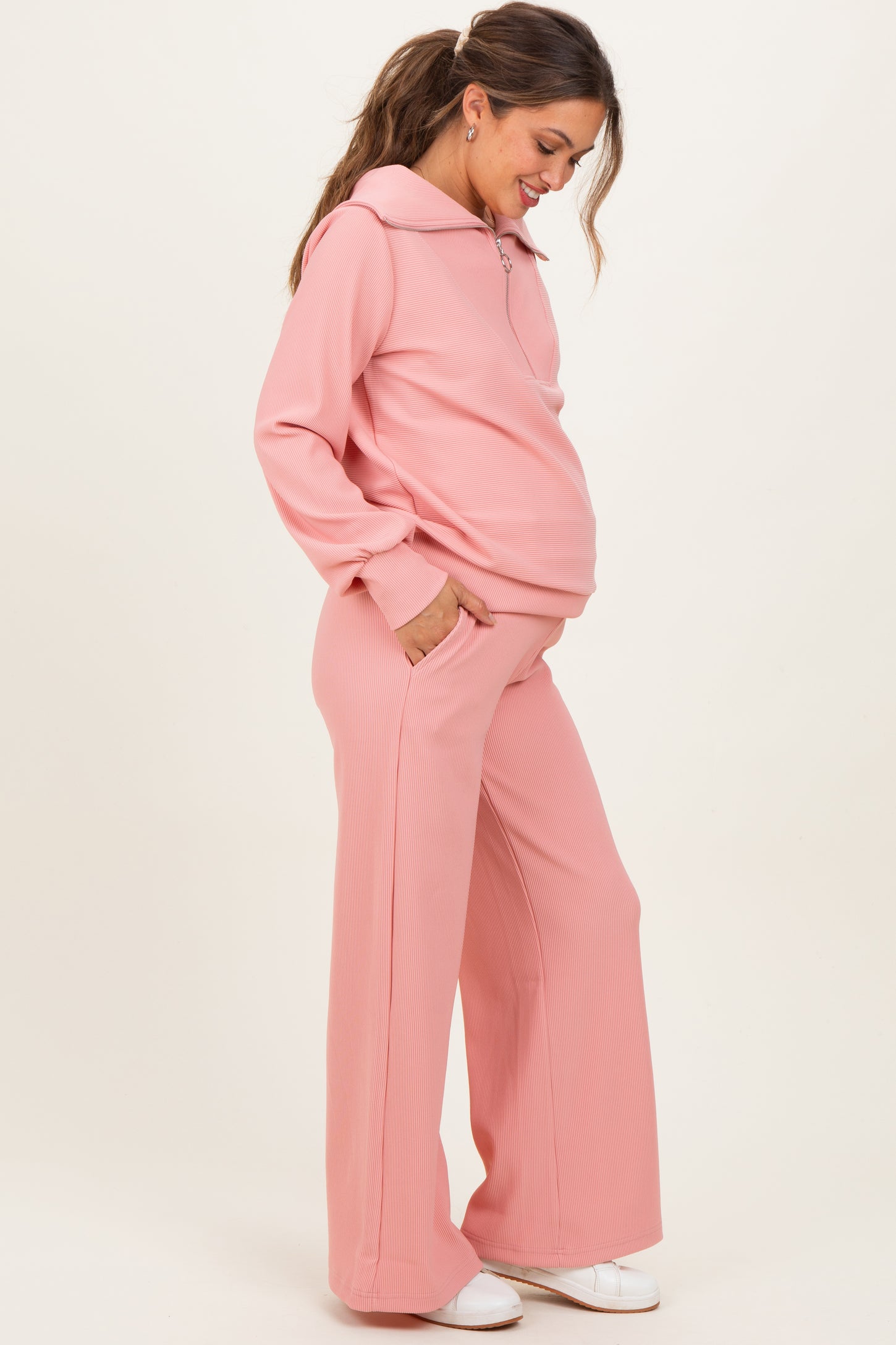 woman wearing a light pink maternity hoodie and matching wide-leg pants, showing her baby bump