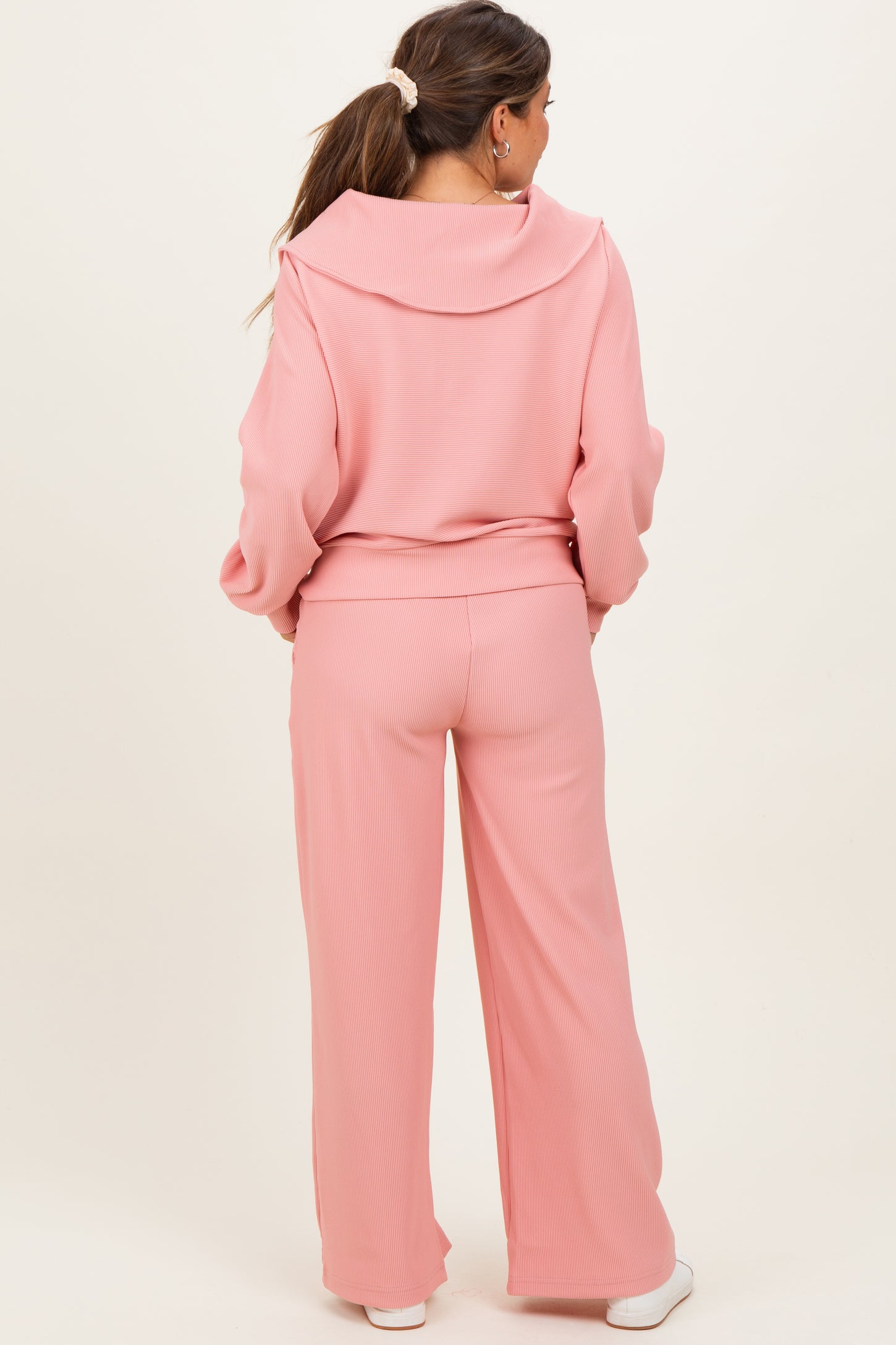 woman wearing a light pink maternity tracksuit with a hooded top and wide-leg pants, showing her baby bump from the back