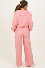 woman wearing a light pink maternity tracksuit with a hooded top and wide-leg pants, showing her baby bump from the back