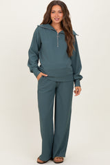 woman wearing a teal maternity tracksuit with a half-zip pullover and wide-leg pants, featuring a stylish collar and pockets