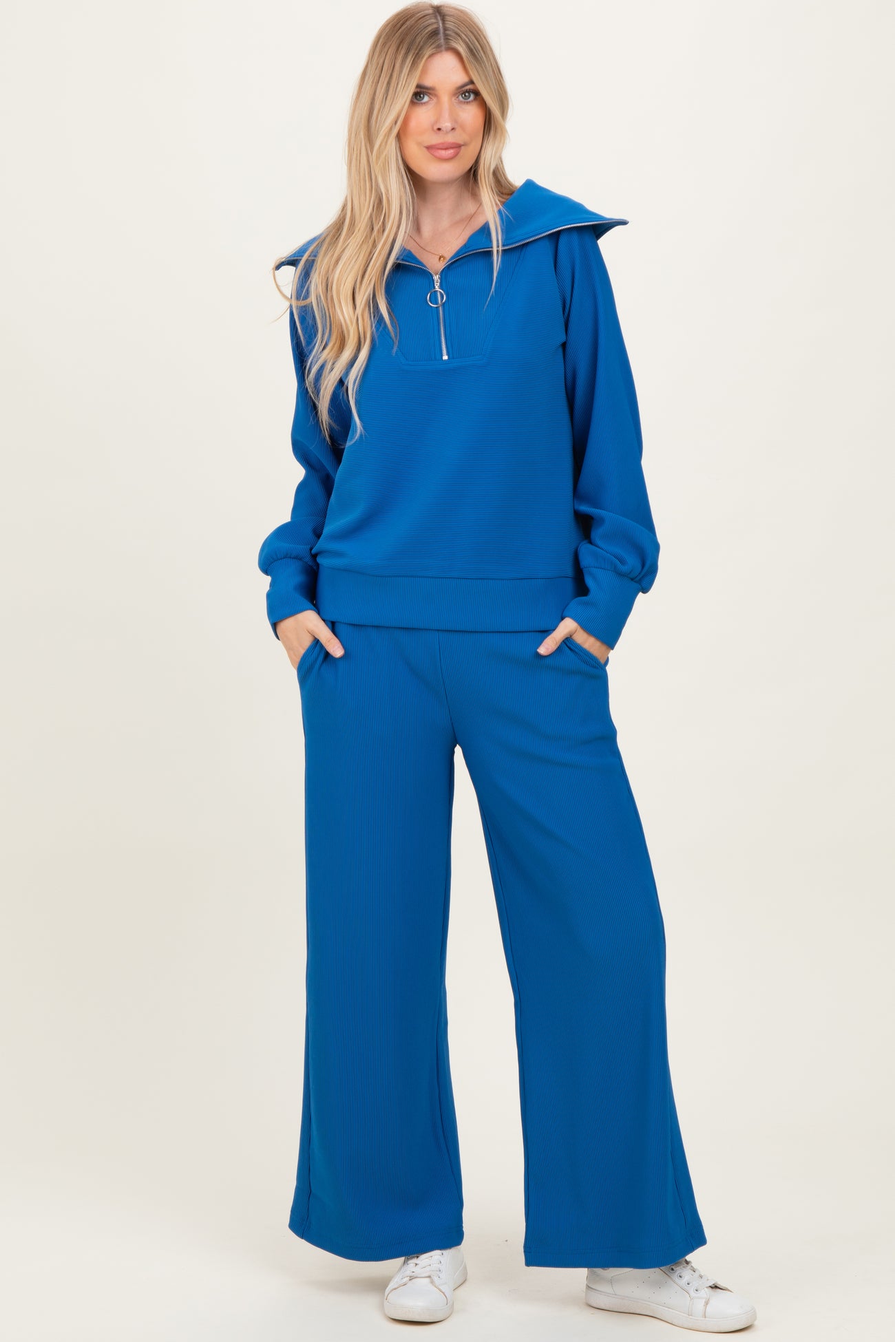 woman wearing a blue ribbed hoodie with a zip and matching wide-leg pants, standing with hands in pockets