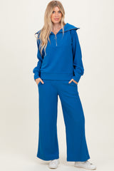 woman wearing a blue ribbed hoodie with a zip and matching wide-leg pants, standing with hands in pockets
