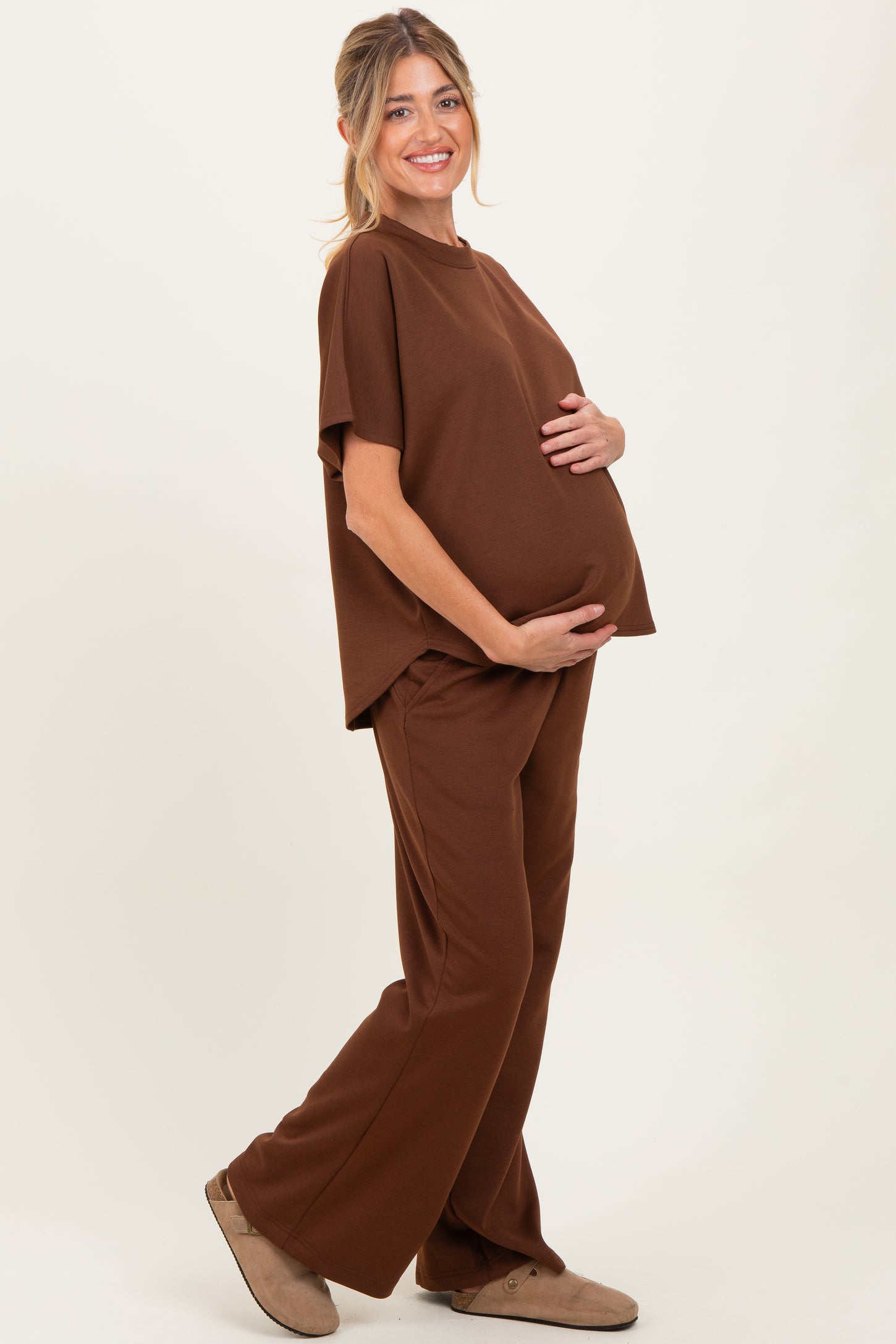 woman wearing a brown short sleeve maternity top and matching pants, holding her baby bump