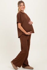 woman wearing a brown short sleeve maternity top and matching pants, holding her baby bump