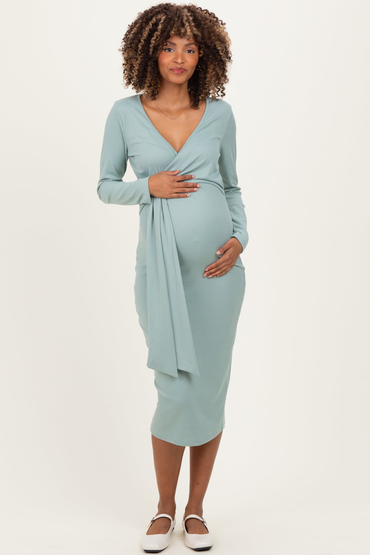 woman wearing a light blue maternity wrap dress with long sleeves, gently holding her baby bump