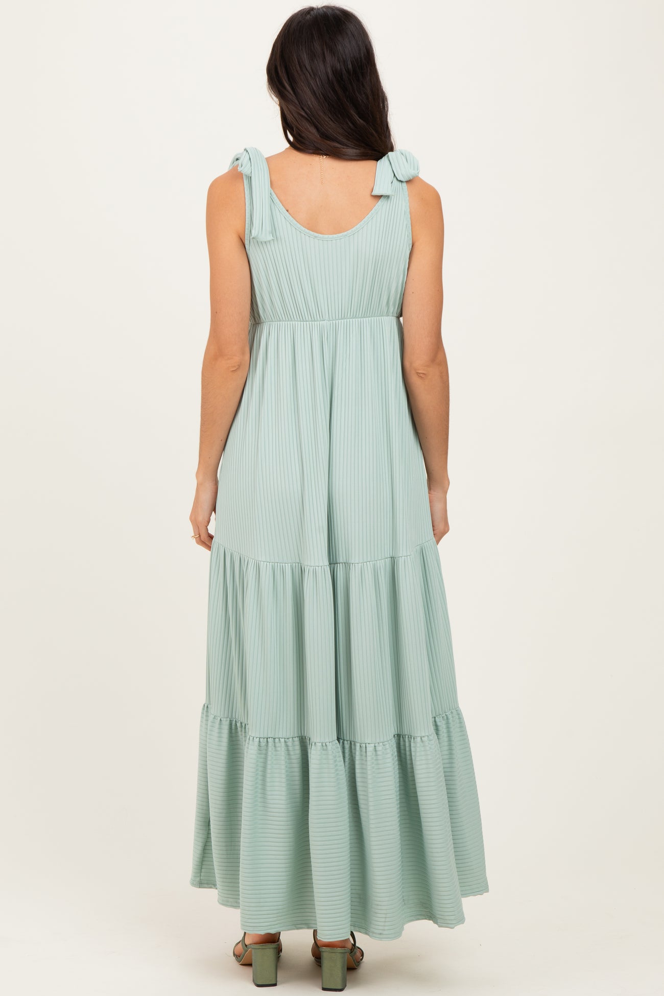 woman wearing a light green striped maxi dress with tie shoulder straps and a tiered skirt, viewed from the back