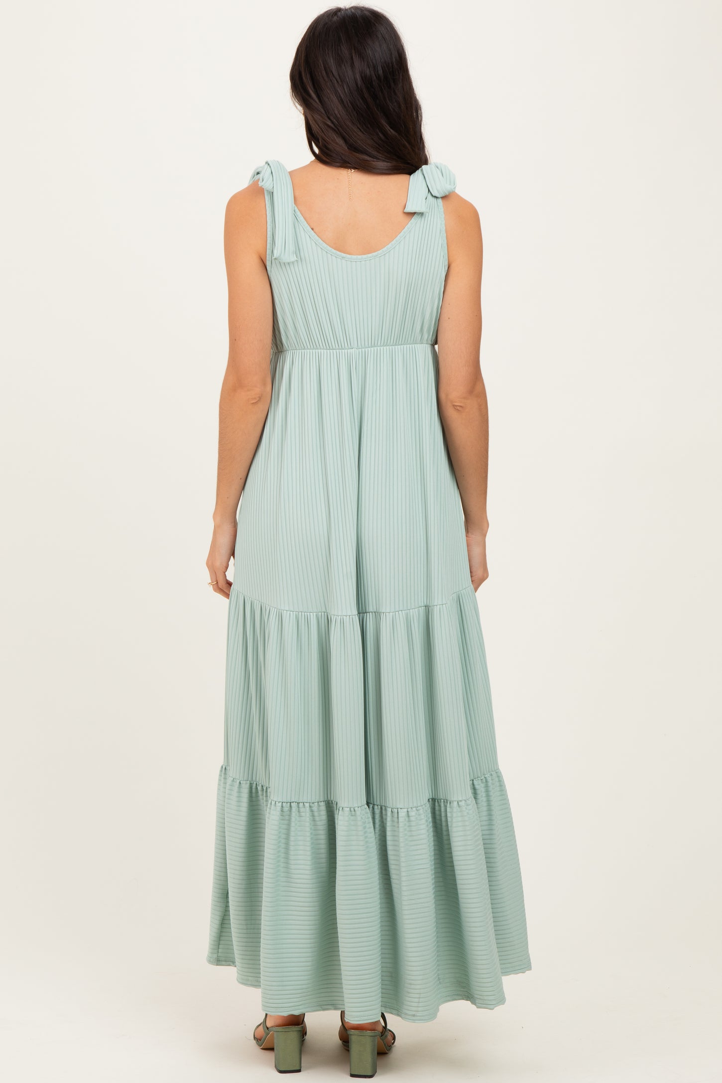 woman wearing a light green striped maxi dress with tie shoulder straps and a tiered skirt, viewed from the back