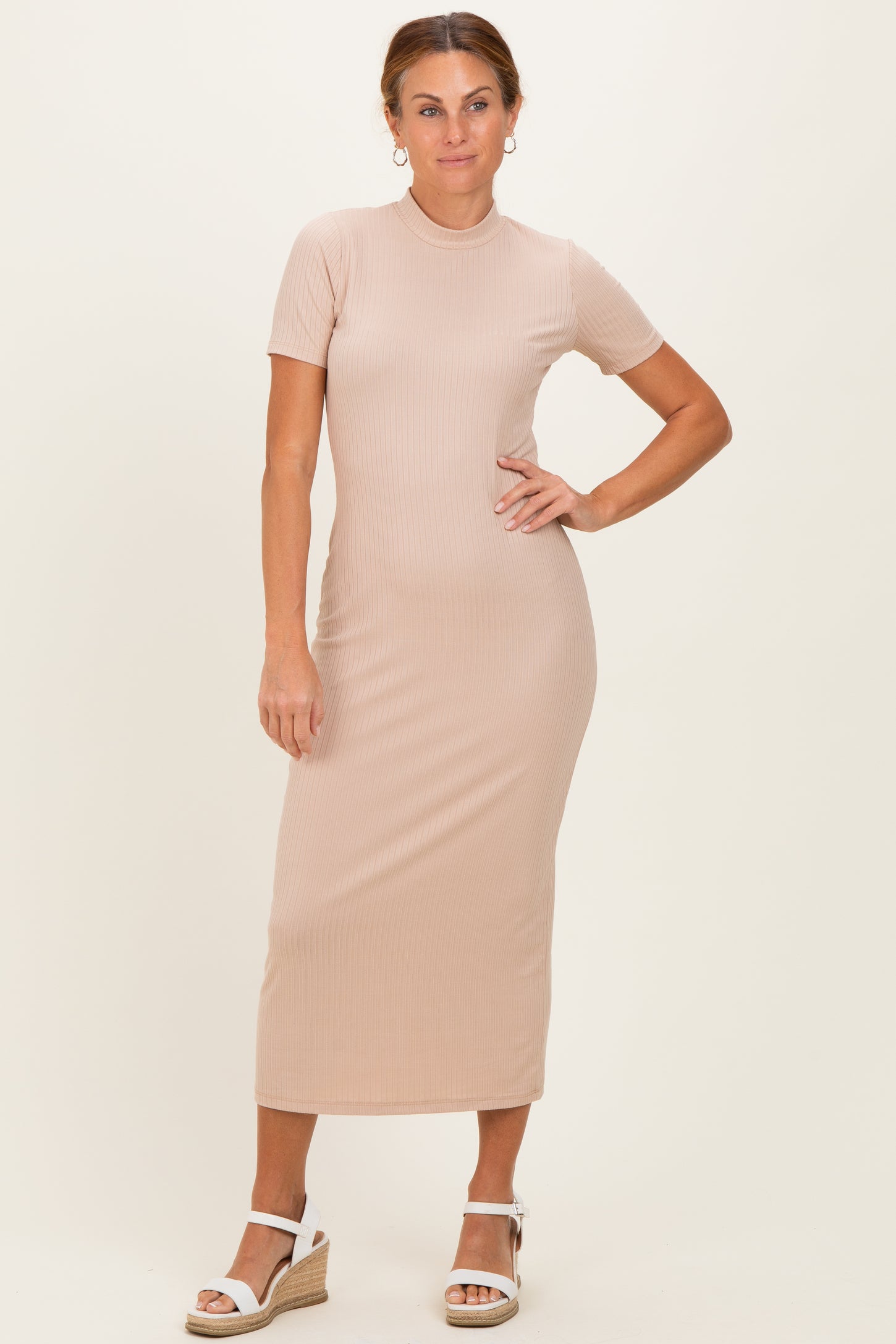 woman wearing a beige ribbed midi dress with short sleeves and a bodycon fit, standing with one hand on her hip