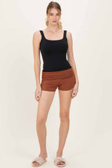 woman wearing a black tank top and rust colored shorts, standing with casual slippers on