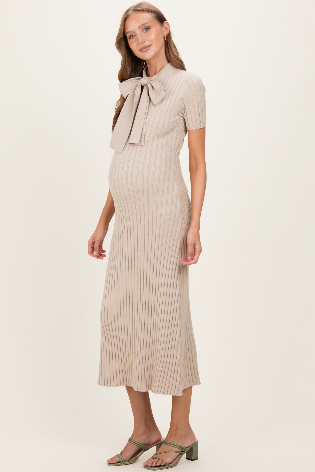 woman wearing a beige ribbed maternity dress with a bow collar and a visible baby bump