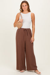woman wearing a white sleeveless top and brown striped wide-leg pants, holding a beige woven bag