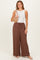 woman wearing a white sleeveless top and brown striped wide-leg pants, holding a beige woven bag