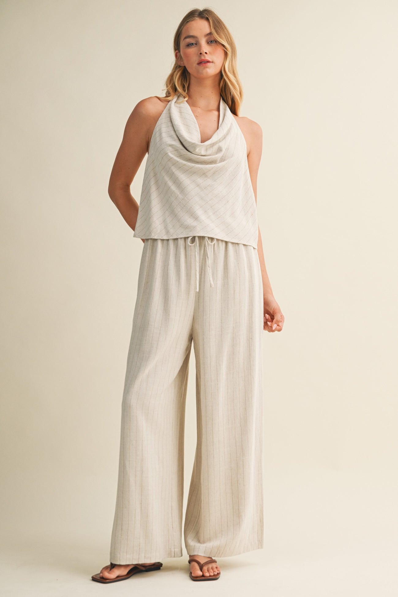 woman wearing a light beige sleeveless top with cowl neck and matching wide-leg pants
