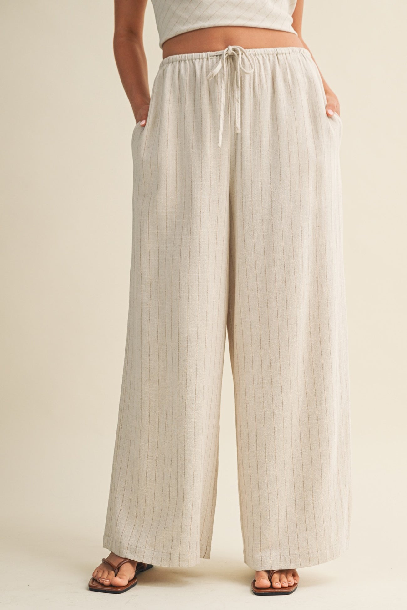 woman wearing cream wide-leg striped pants with an elastic waistband and pockets, styled with a cropped top