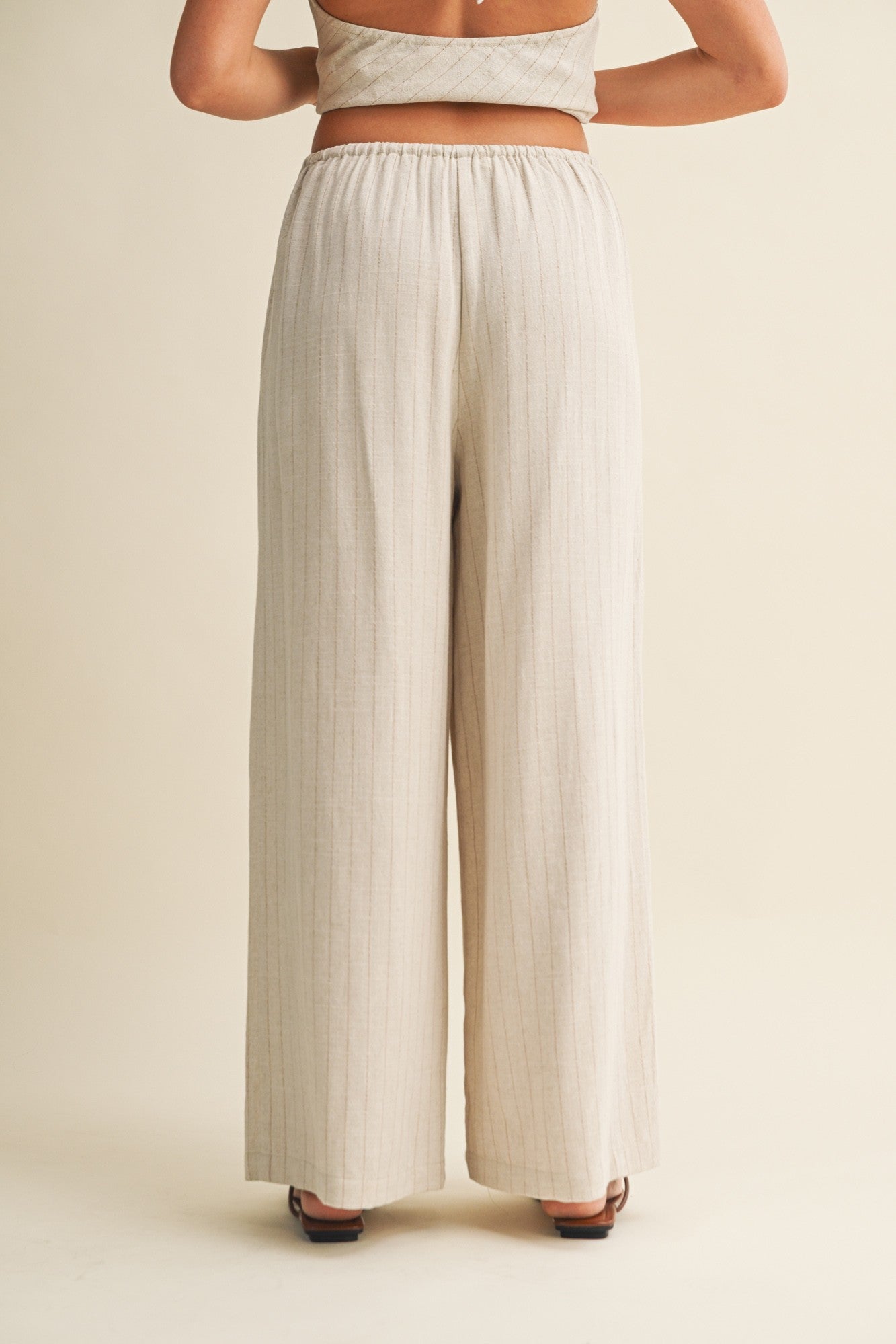 woman wearing beige high-waisted wide-leg pants with vertical stripes, viewed from the back