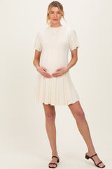 woman wearing a cream short sleeve maternity dress, holding her baby bump with a pleated skirt detail