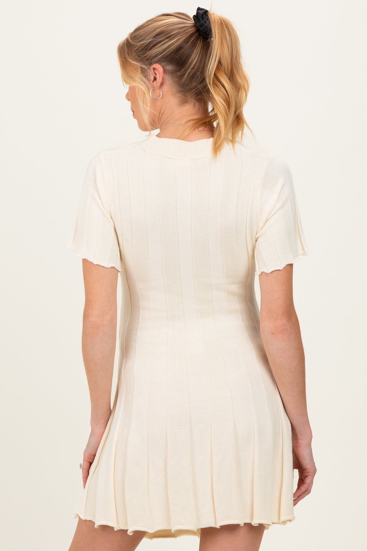 woman wearing a cream short sleeve ribbed maternity dress with a flared hemline, showing no baby bump