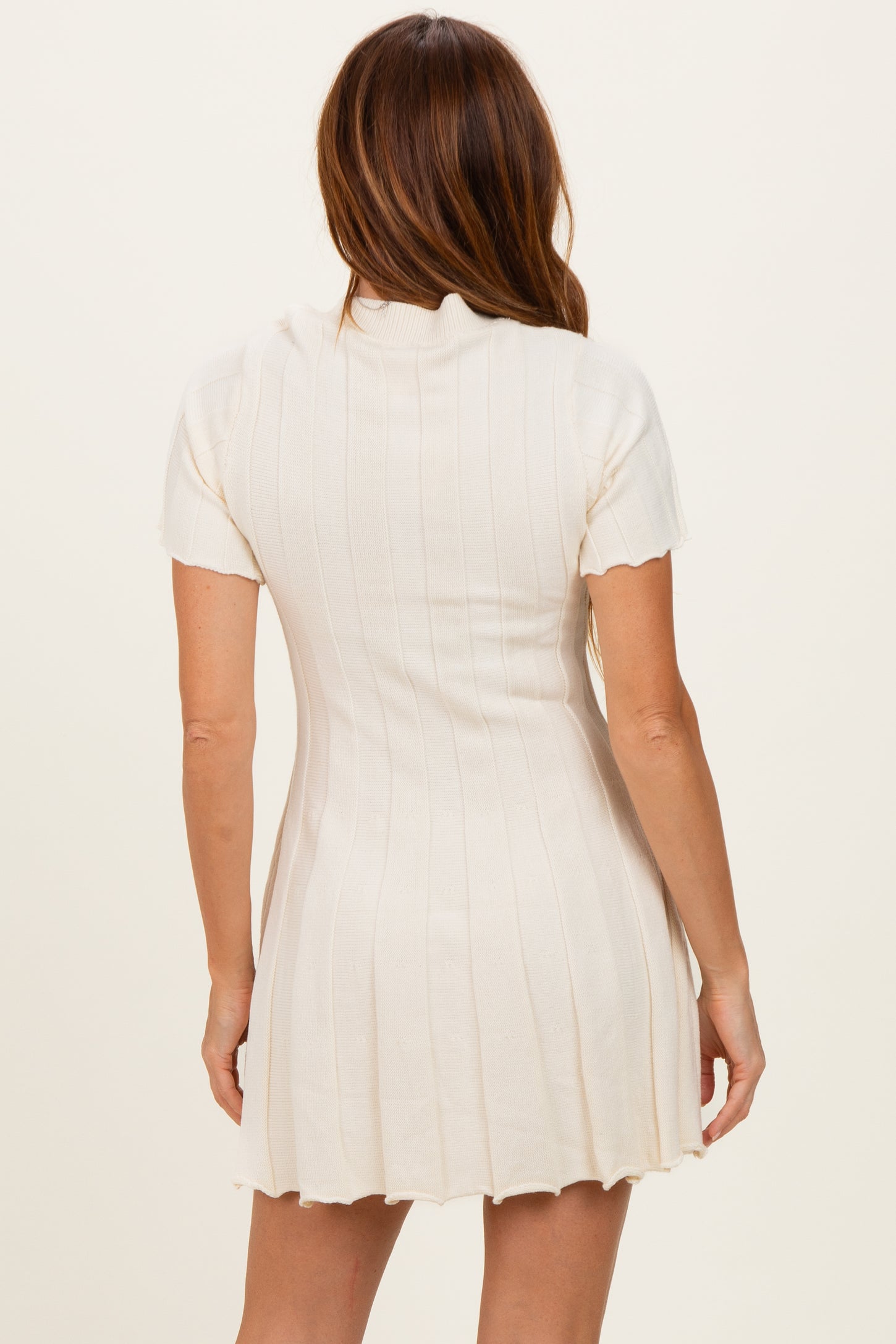 woman wearing a cream short sleeve ribbed knit dress with a fitted silhouette and flared hem