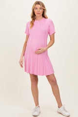 woman wearing a pink short sleeve maternity dress with a pleated skirt and holding her baby bump
