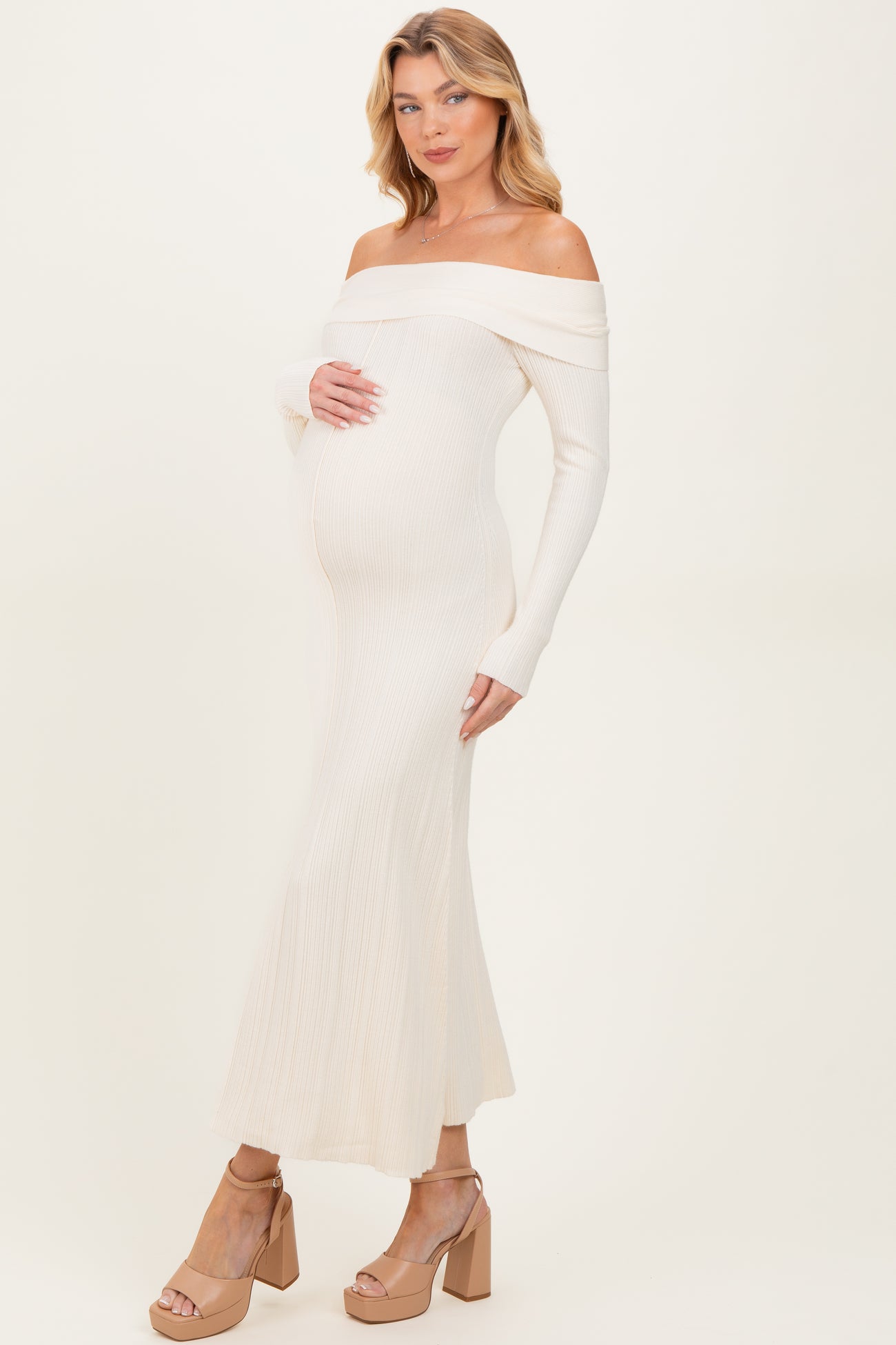 woman wearing a cream off-shoulder ribbed maternity dress and showing her baby bump
