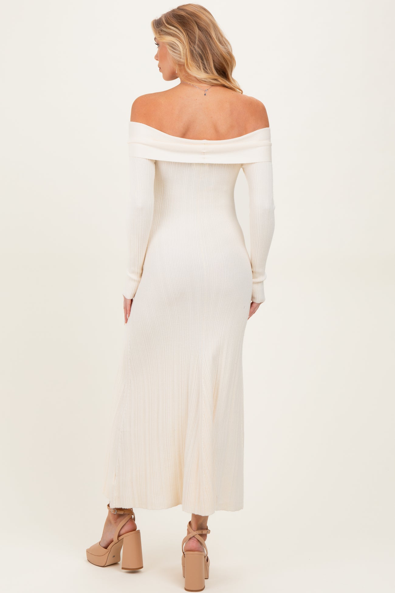 woman wearing a cream off-the-shoulder ribbed maternity dress with long sleeves and a flowing midi length
