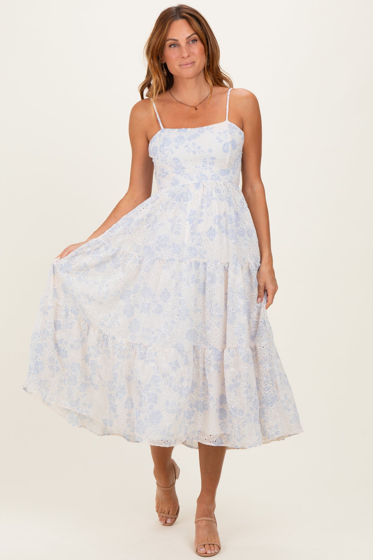 woman wearing a light blue floral midi dress with spaghetti straps and tiered design, standing and smiling