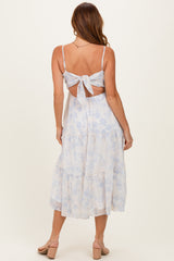 woman wearing a light blue floral midi dress with a tie-back detail and tiered skirt, shown from the back