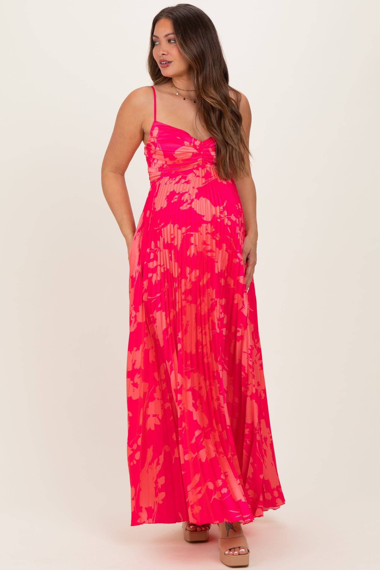 woman wearing a pink floral print maternity maxi dress with spaghetti straps and a pleated skirt