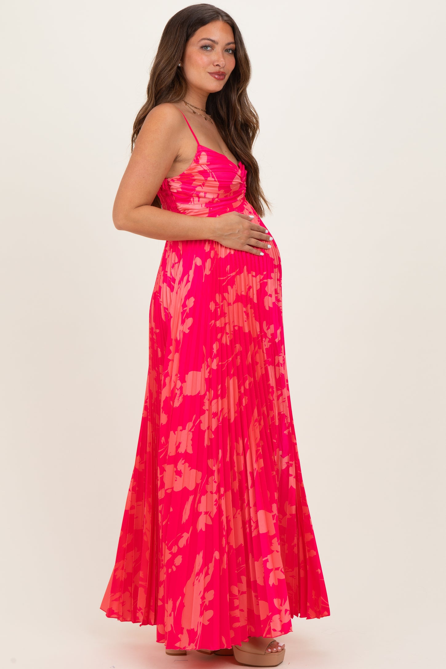 woman wearing a bright pink floral printed maternity maxi dress and holding her baby bump