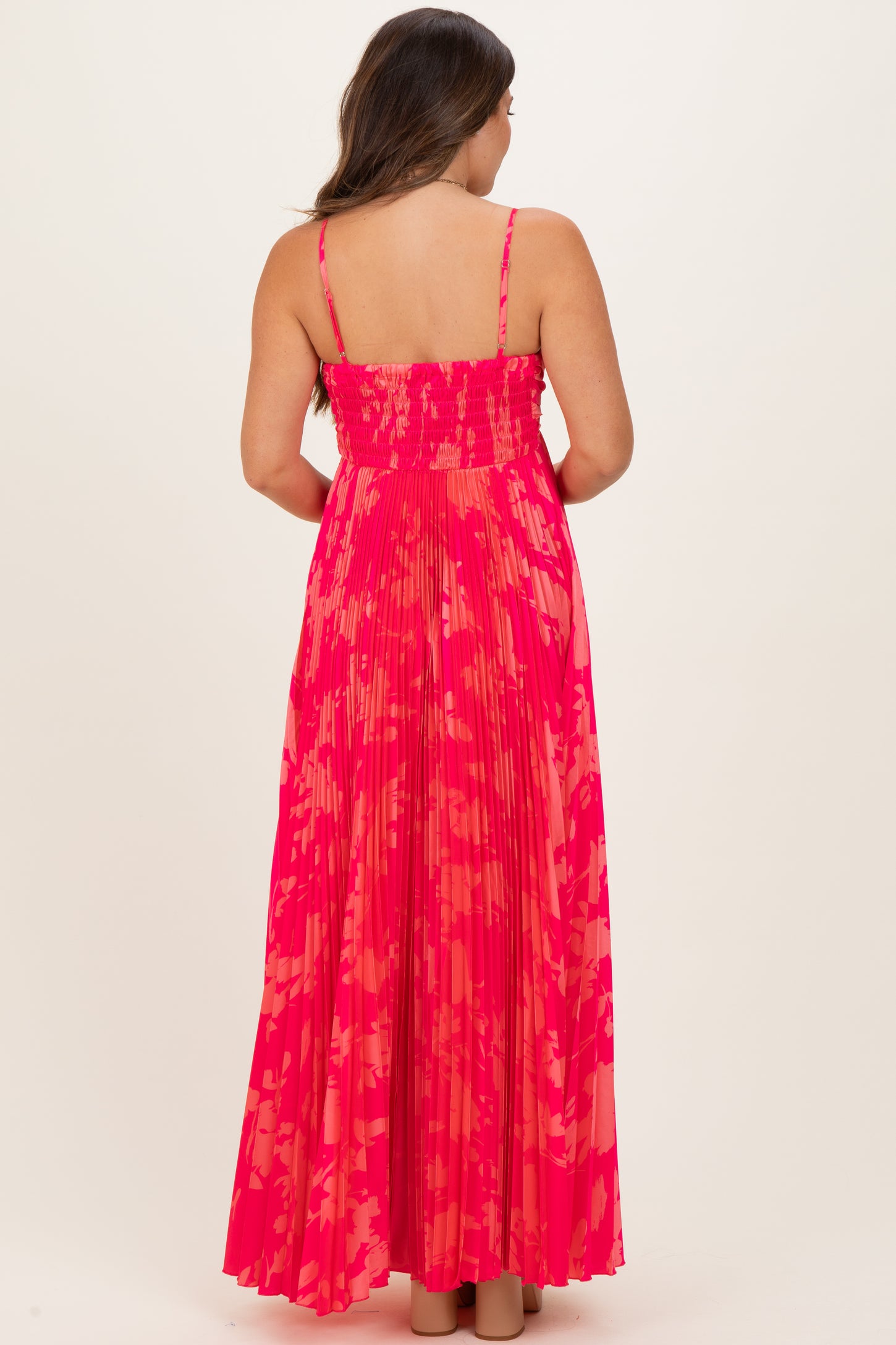 woman wearing a pink and coral patterned maternity maxi dress with a smocked bodice and pleated skirt, showing a baby bump