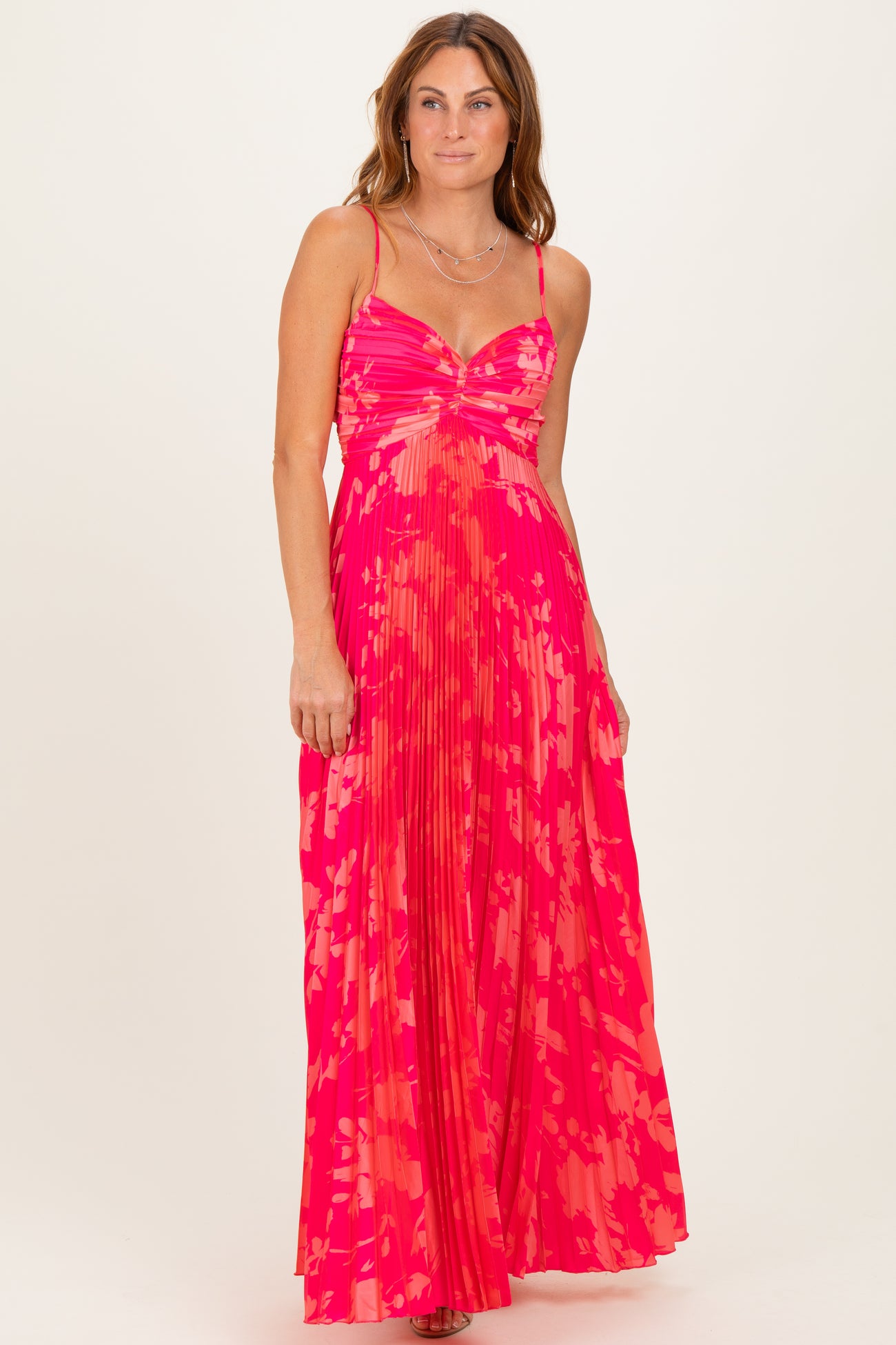 woman wearing a bright pink pleated maxi dress with a twist bodice and spaghetti straps