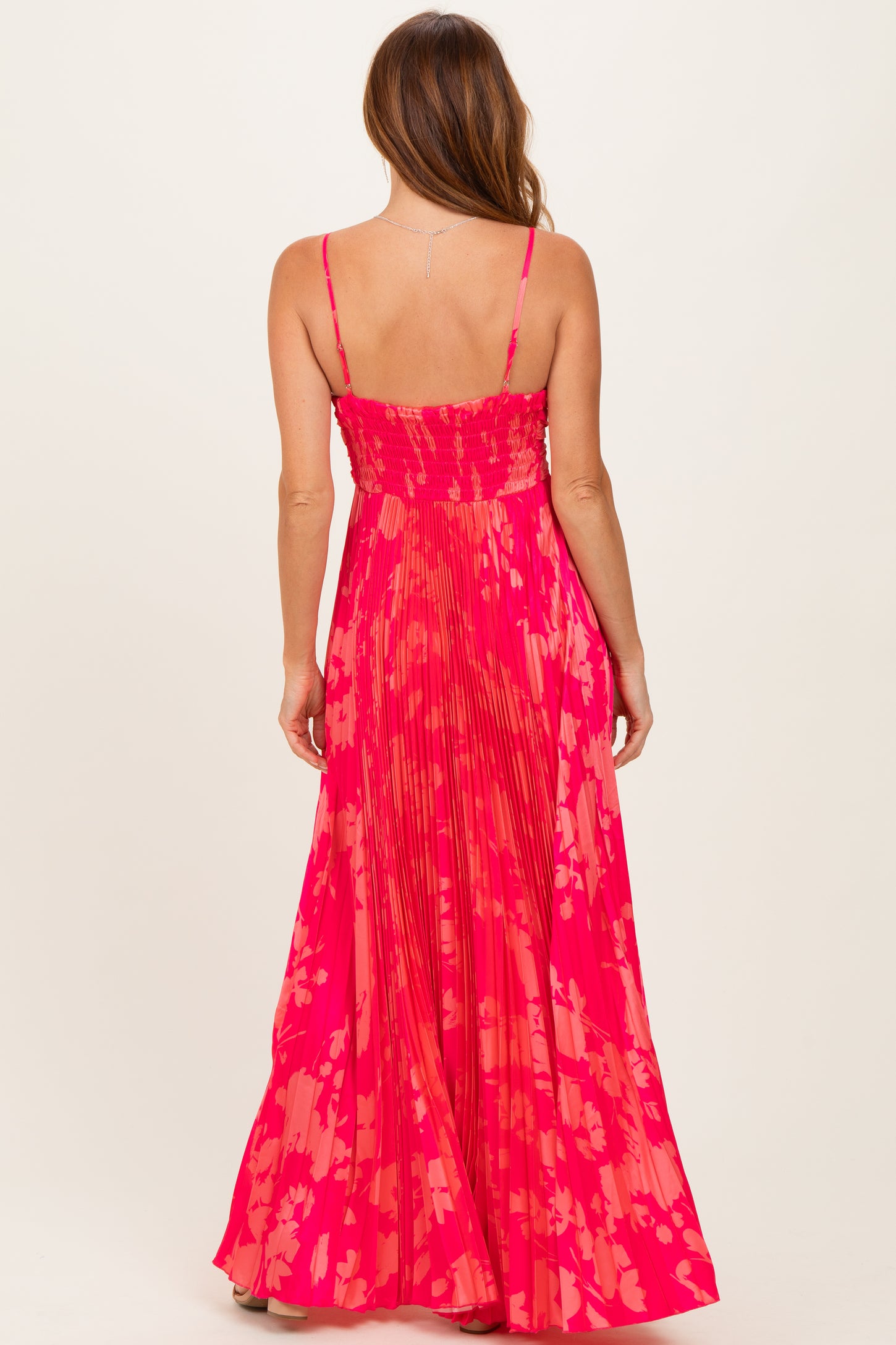 woman wearing a vibrant pink floral maxi dress with a smocked back and flowing pleated skirt