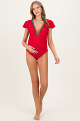 woman wearing a red maternity swimsuit with flutter sleeves and colorful embellishments, gently holding her baby bump