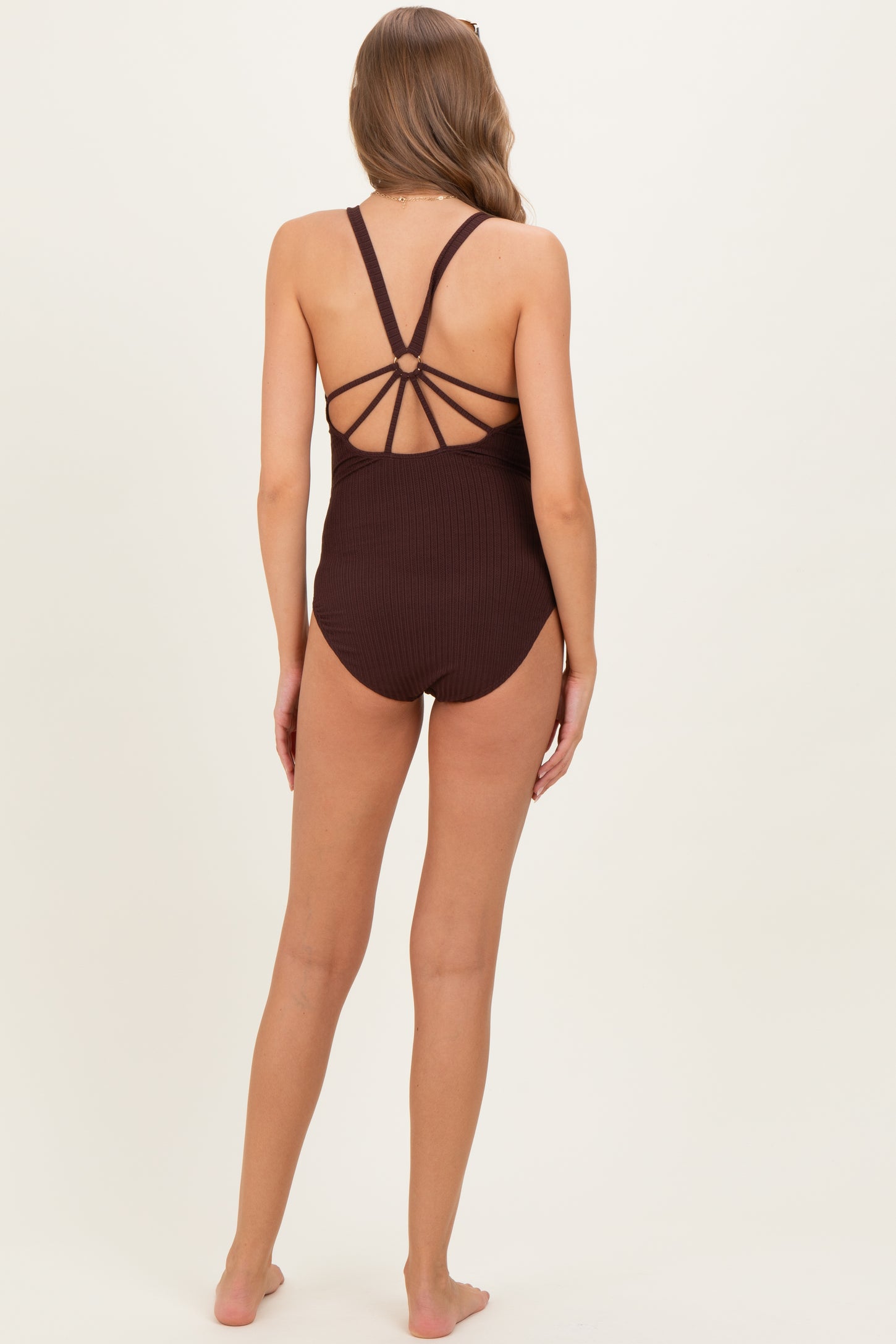 woman wearing a brown ribbed maternity swimsuit with a strappy back design and no visible baby bump