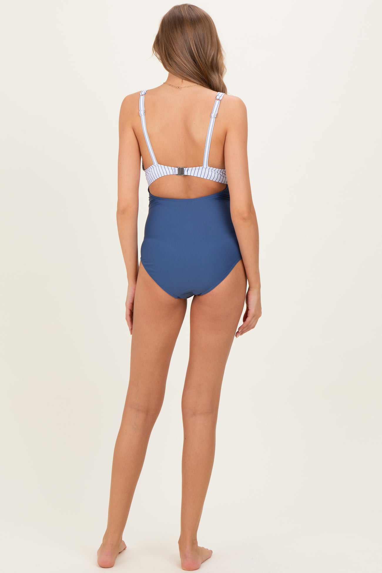 woman wearing a navy blue maternity swimsuit with striped straps and a clasp back detail