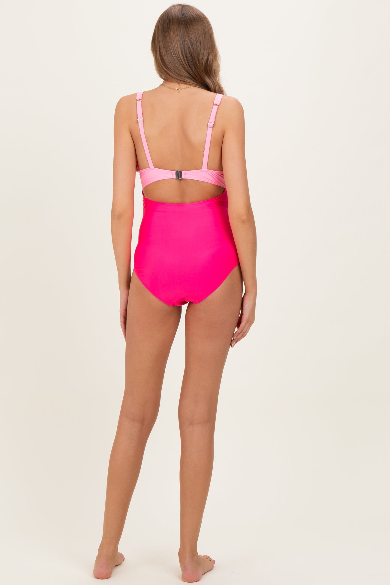 woman wearing a hot pink maternity swimsuit with adjustable straps and a back cutout detail
