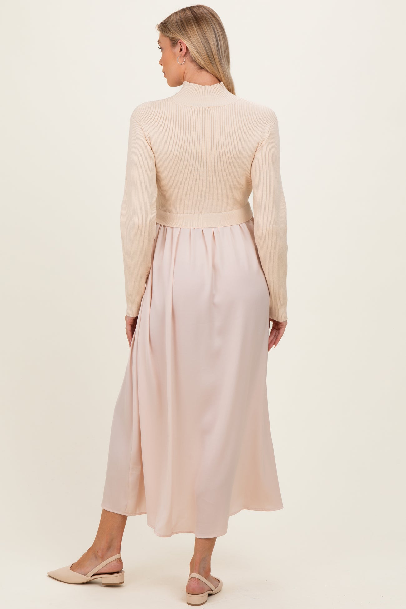 woman wearing a beige maternity dress with a fitted knitted top and flowing silk-like skirt, showing her baby bump