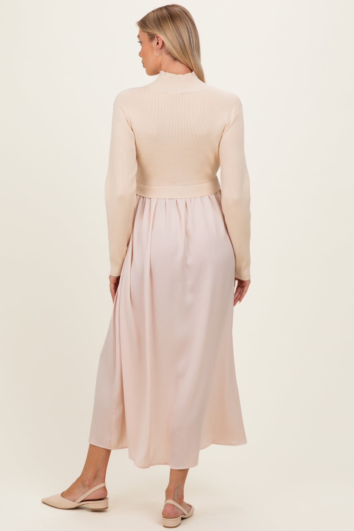 woman wearing a beige maternity dress with a fitted knitted top and flowing silk-like skirt, showing her baby bump