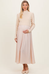 woman wearing a cream ribbed maternity sweater and a pale pink maxi skirt, gently holding her baby bump