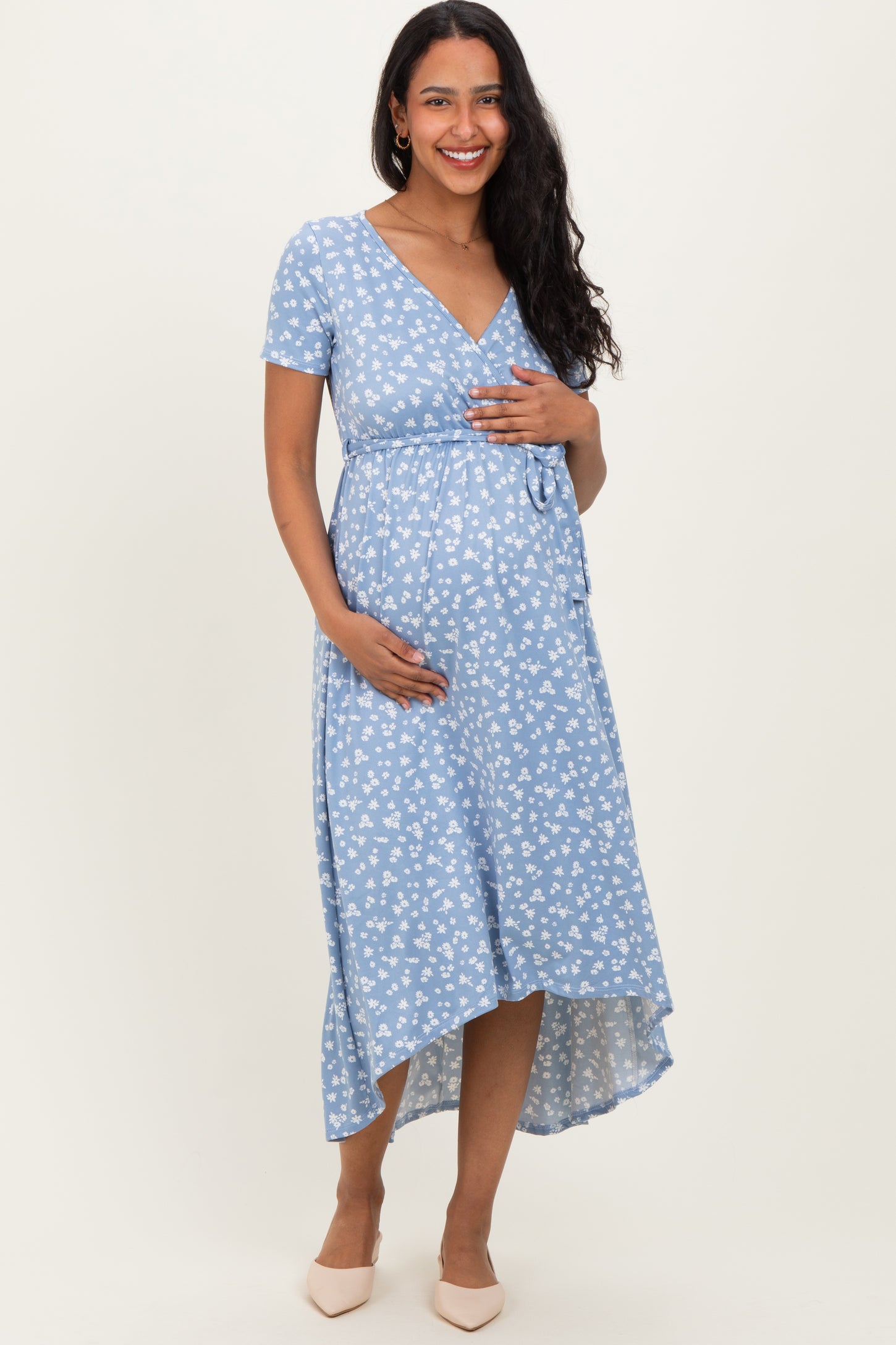 woman wearing a blue floral print maternity dress with short sleeves and a tie waist, holding her baby bump