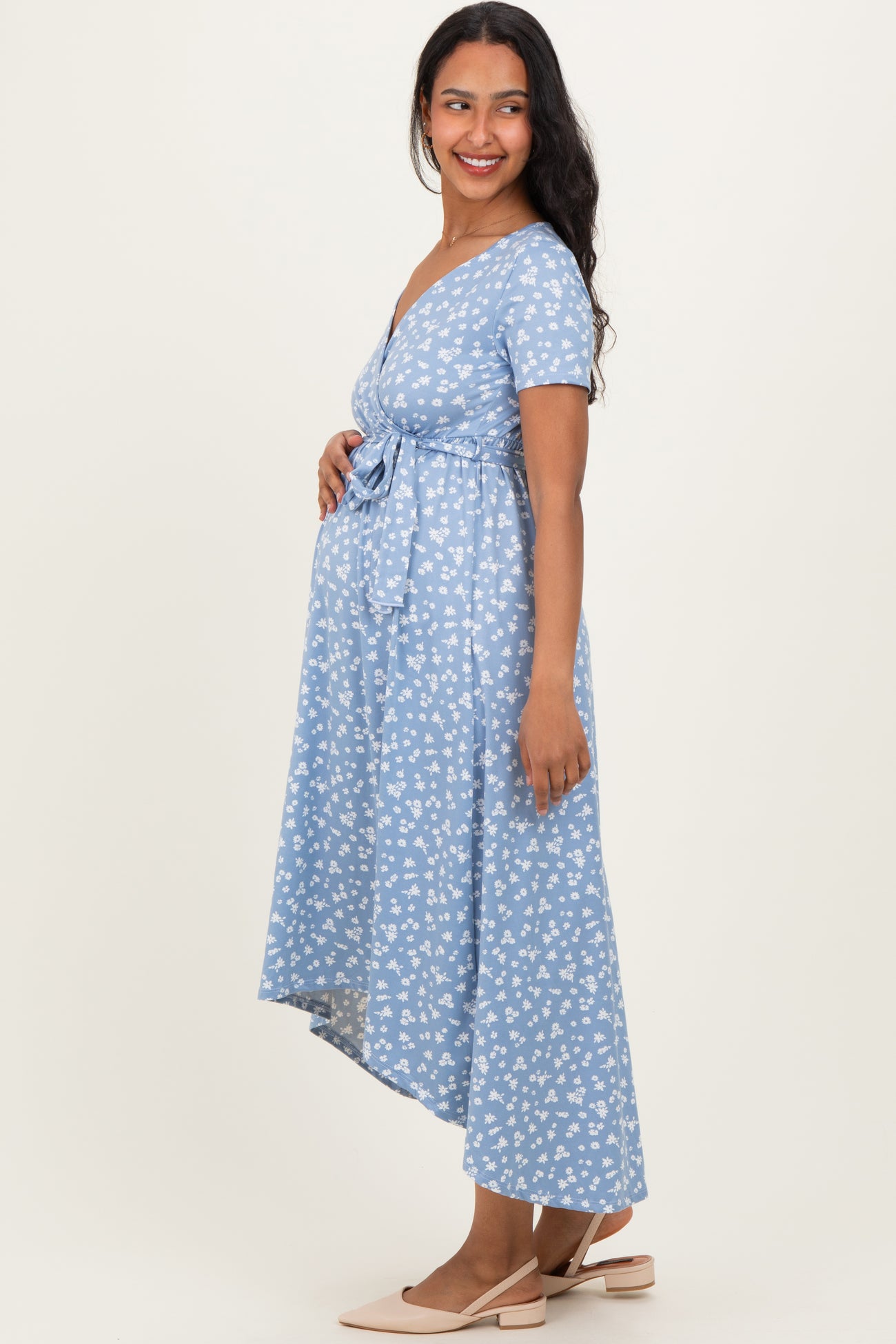 woman wearing a light blue floral maternity dress with a tie waist and an asymmetrical hem, showcasing her baby bump