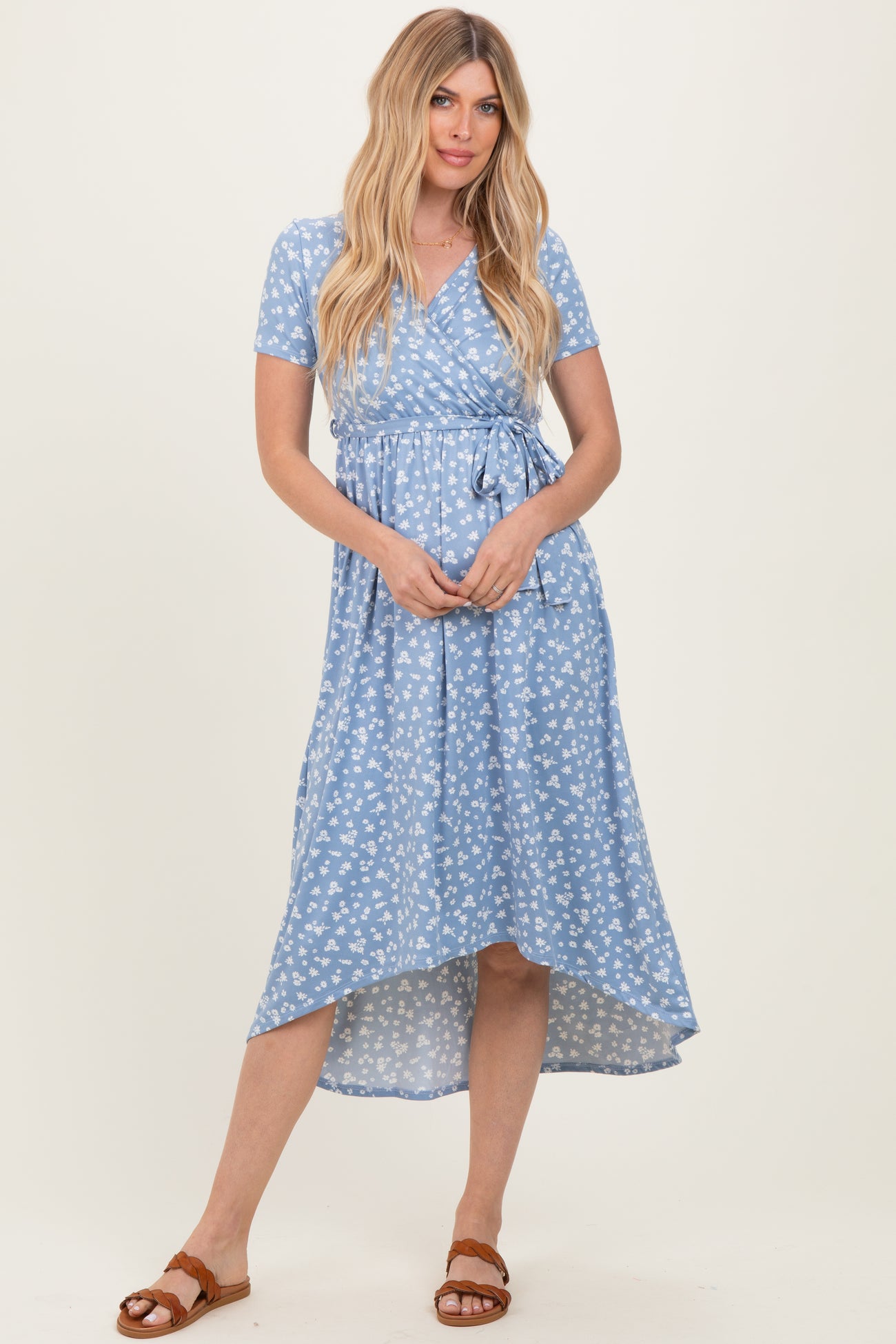 woman wearing a light blue wrap dress with white floral print and short sleeves, standing and smiling